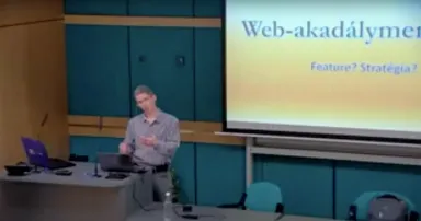 Előadóteremben Edelényi Zsolt prezentál, a kivetítőn a "Web-akadálymentesség: Feautre? Stratégia?" felirat.