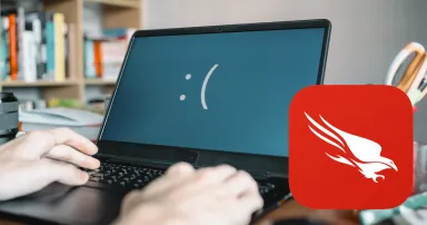 Kék halál a laptopon, előtte pedig a CrowdStrike Falcon logója.