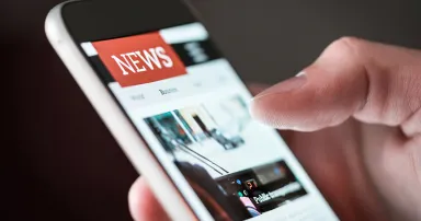 Mobile news application in smartphone. Man reading online news on website with cellphone. Person browsing latest articles on the internet. Light from phone screen.