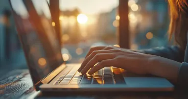 Close up of female hands typing on laptop keyboard, working at home, sunset in background