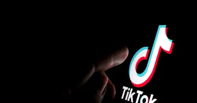 TikTok app logo on the screen and a finger about to touch it.