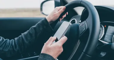 Texting and driving is dangerous behavior in traffic, close up of female hand typing text message on mobile phone while traveling through countryside with her car