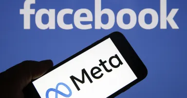 A Meta logo is seen on a smartphone in front of a Facebook logo