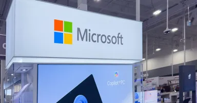 A brightly lit Microsoft display in a retail environment showcases Surface Pro devices and promotes "Copilot+ PC."