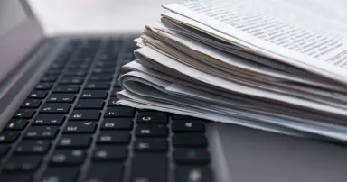 Pile of daily papers with news on the computer