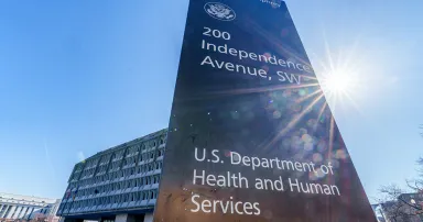 The sun flares next to the sign marking the headquarters building of the US Department of Health and Human Services