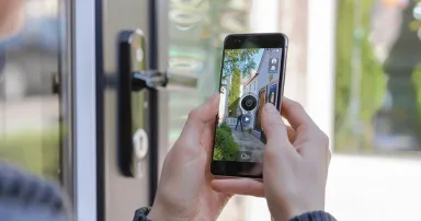 Hands holding a smartphone displaying the interface and video feed of a doorbell camera. the smart device showcases real-time surveillance footage, emphasizing modern home security solutions. essential technology for monitoring and ensuring safety at home.