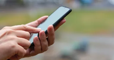 Male hand holding smart phone outside.