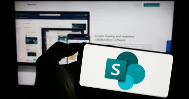 Person holding smartphone with logo of collaborative platform Microsoft SharePoint on screen in front of website. Focus on phone display.