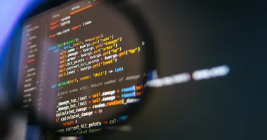 Colorful lines of code seen through a magnifying glass on a dark screen, symbolizing careful debugging, code review, and detailed software quality analysis