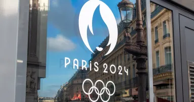 The interconnected rings of the Olympics logo and a design of the Olympic flame with the words Paris 2024 are seen on a window