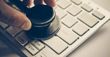 hand holding a stethoscope over computer keyboard