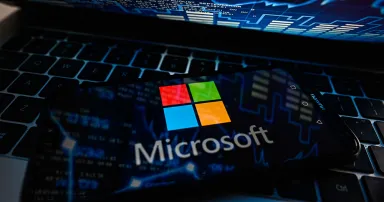 A Microsoft logo is displayed on a smartphone on top of a laptop keyboard.