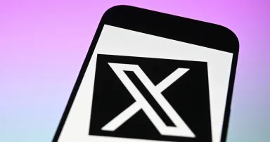 The logo of 'X' (formerly known as Twitter) is displayed on a mobile phone screen in front of a computer screen. (Photo by Ismail Kaplan/Anadolu via Getty Images)