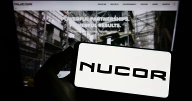 Person holding smartphone with logo of US steel company Nucor Corporation on screen in front of website. Focus on phone display.