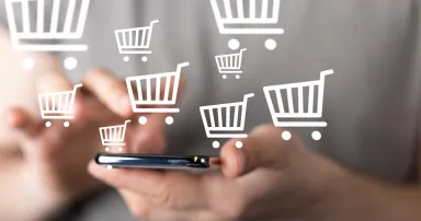 A man holds a smartphone with checkout icons floating around