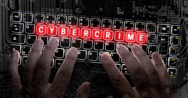 The word "cybercrime" is illuminated in a red on a computer keyboard