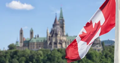 Canadian flag waving with Parliament Buildings hill and Library in the background