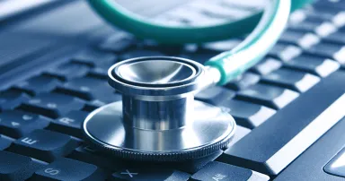 Closeup of a green stethoscope lying on a blue notebook keyboard (selective focus)